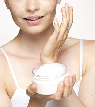 Young woman applying moisturizer to face, portrait